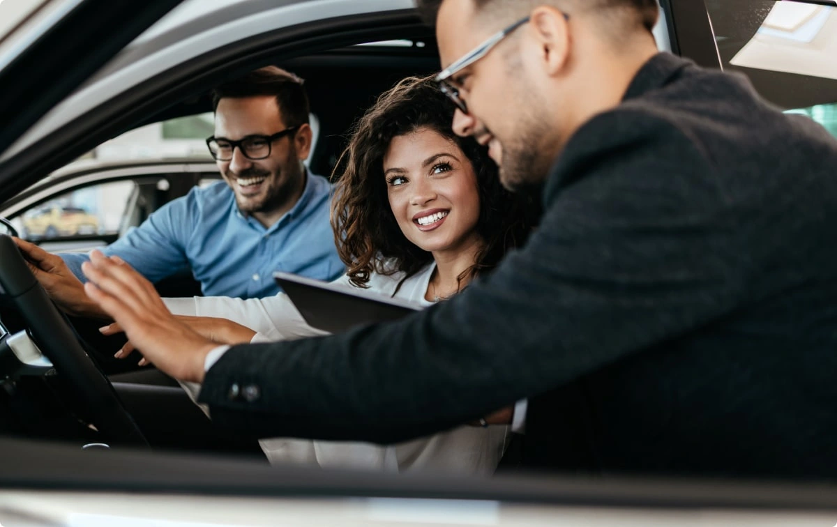 Advisor showing a tablet to a couple seated inside a car during a test drive